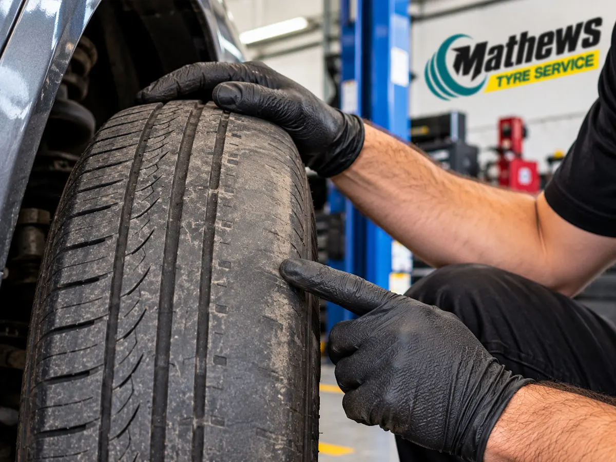 Mechanic inspecting uneven tyre tread wear that may be associated with incorrect tyre pressure.